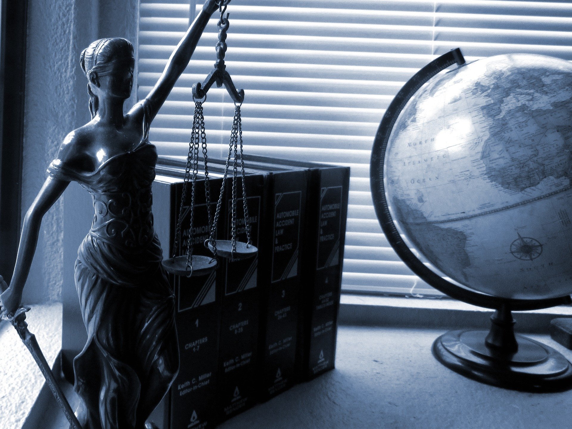 schwarz-weiß Bild mit Justitia mit verbundenen Augen, Büchern und Globus auf Schreibtisch
